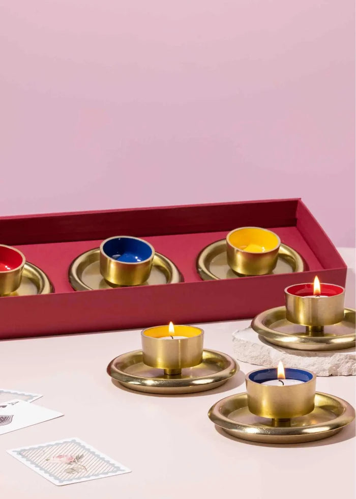 Set of brass candle holders with candles on a pink background