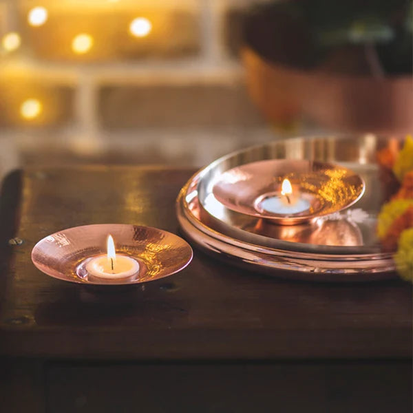Candlelit copper plates on a reflective surface with blurred lights in the background