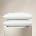 Two white pillows stacked on a beige pedestal against a beige background