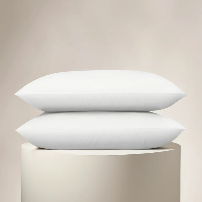 Two white pillows stacked on a beige pedestal against a beige background