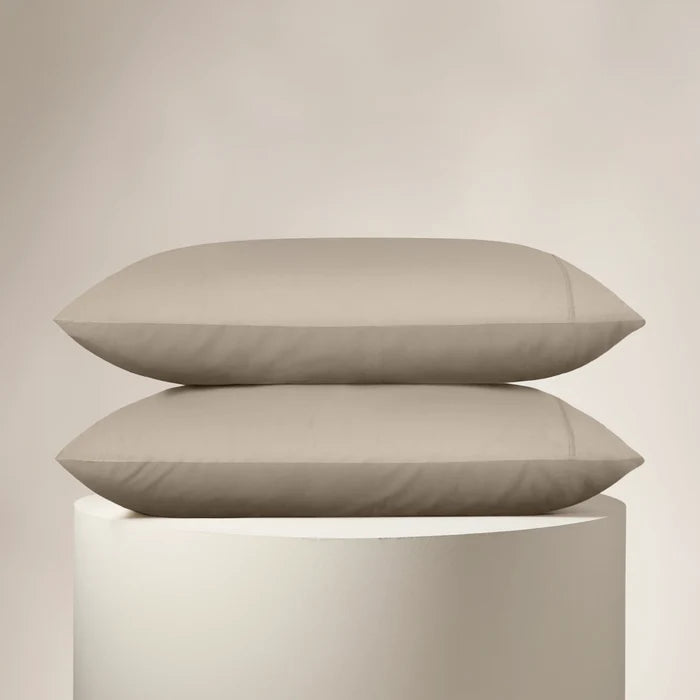 Two beige pillows stacked on a cylindrical white stand against a beige background
