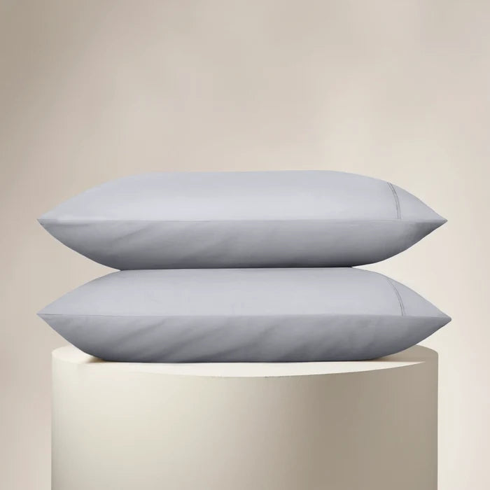 Two light gray pillows stacked on a beige pedestal against a beige background