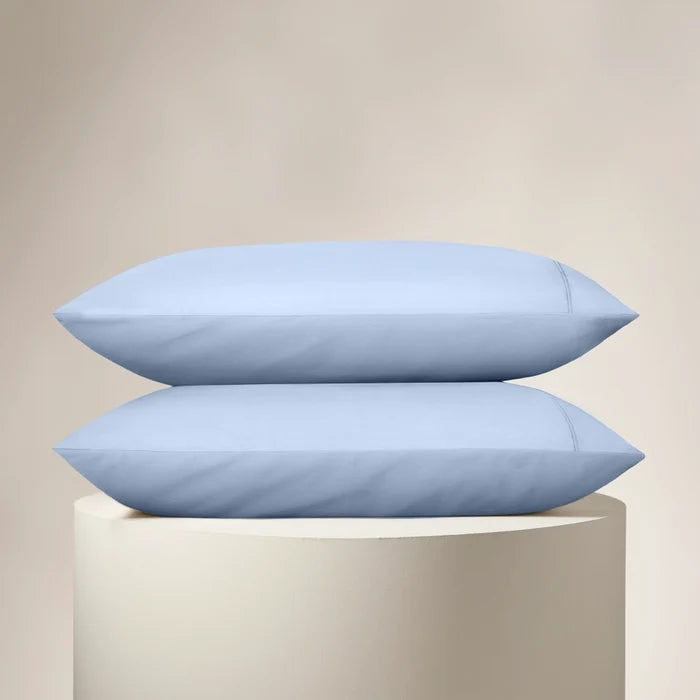 Two light blue pillows on a beige pedestal against a beige background