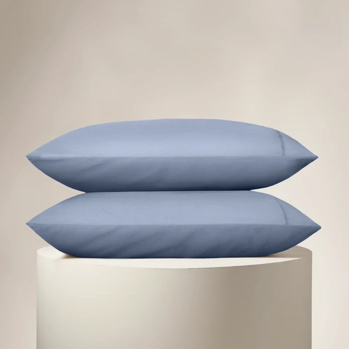 Two blue pillows stacked on a white pedestal against a beige background