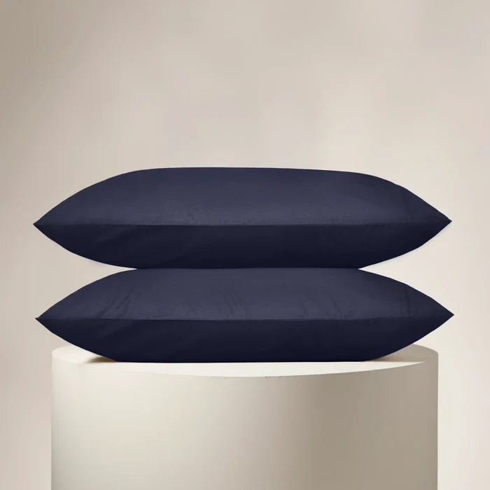 Two navy blue pillows stacked on a white pedestal against a beige background