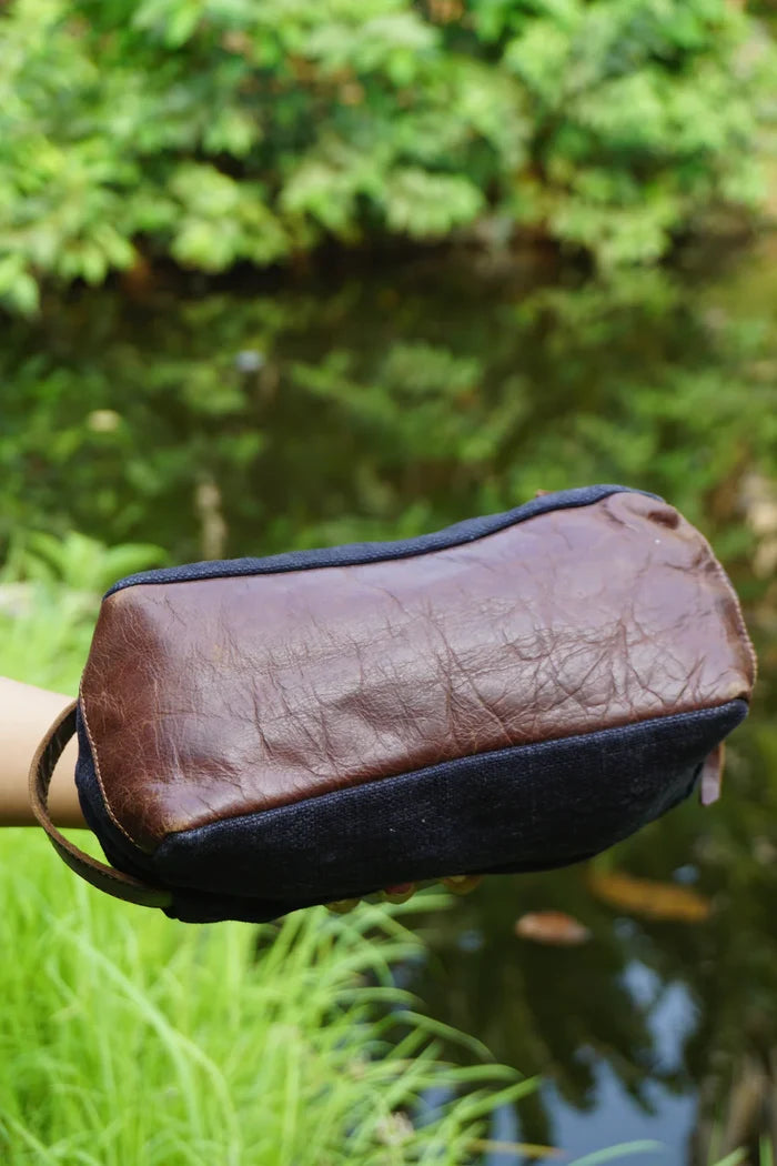 Brown leather pouch held in front of a blurred natural background