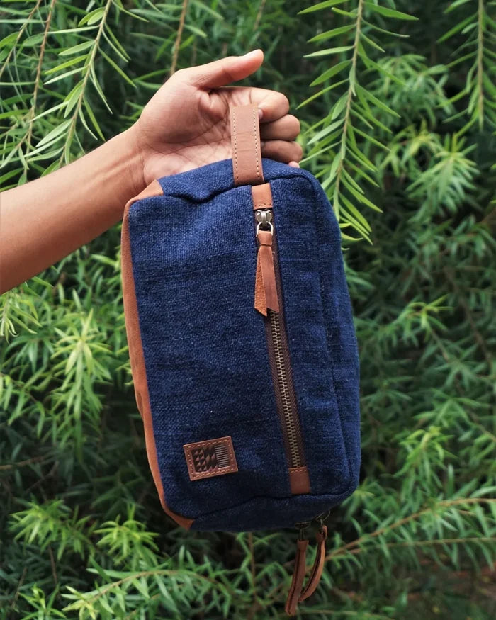 Blue textured pouch with brown leather accents held against a green leafy background