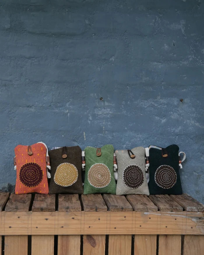 Five colorful pouches with circular patterns on a wooden surface against a blue wall.