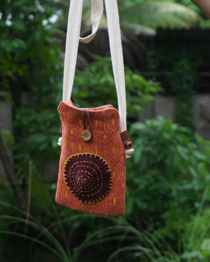 Small orange bag with a circular design hanging against a green, blurred natural background