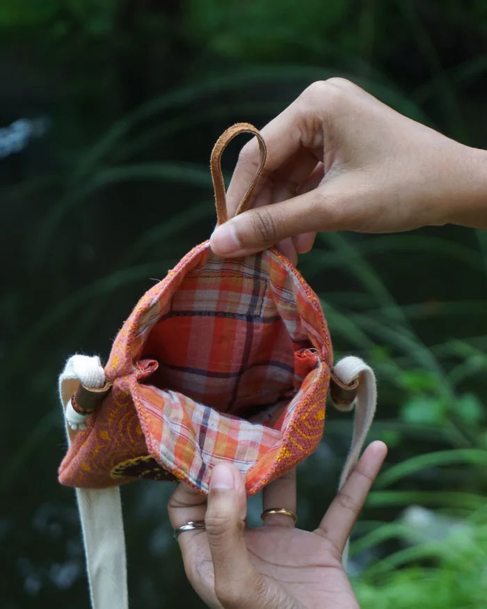 Hand holding a small fabric pouch with plaid interior against a natural background