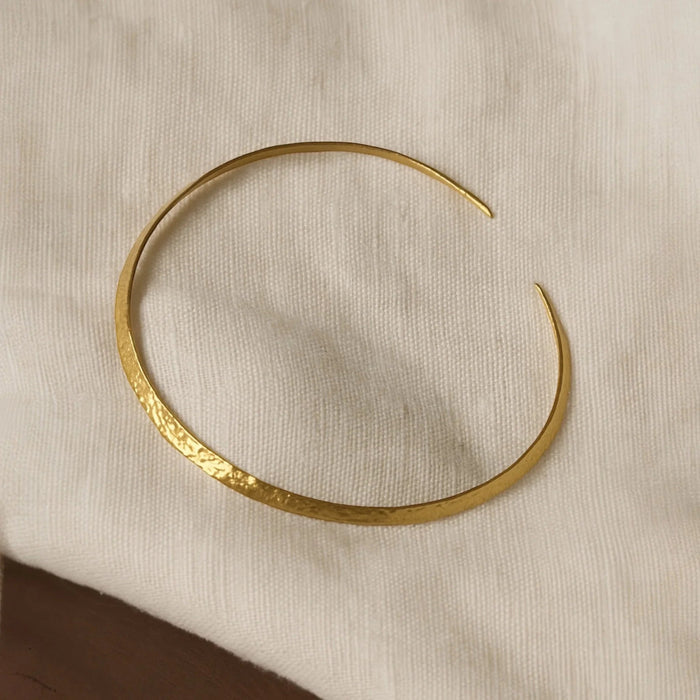 Nærbilde av Kura choker, håndlaget gullsmykke i forgylt messing med hamret tekstur.