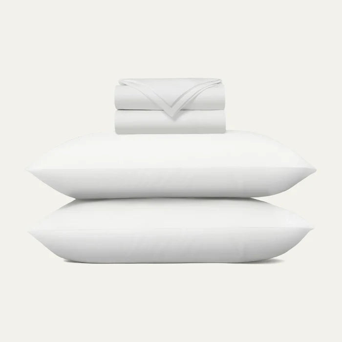 Set of white pillows and a folded blanket on a light gray background