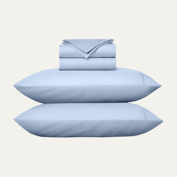 Set of light blue bedding including pillows and a folded sheet on a white background