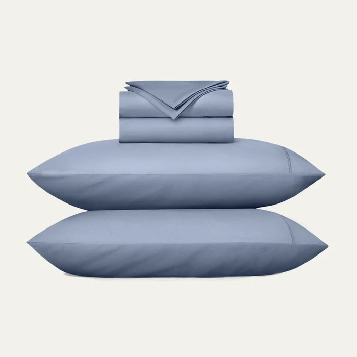 Blue bedding set with two pillows and a folded sheet on a white background