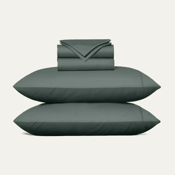 Set of green bedding including a duvet, two pillows, and a folded sheet on a light gray background.