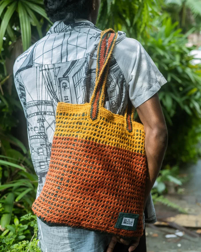 Person holding a crocheted bag with orange and yellow gradient in a natural setting