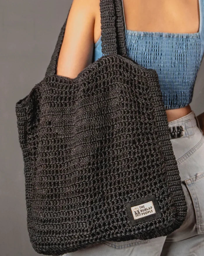 Person holding a dark gray crochet bag with a visible brand label against a neutral background