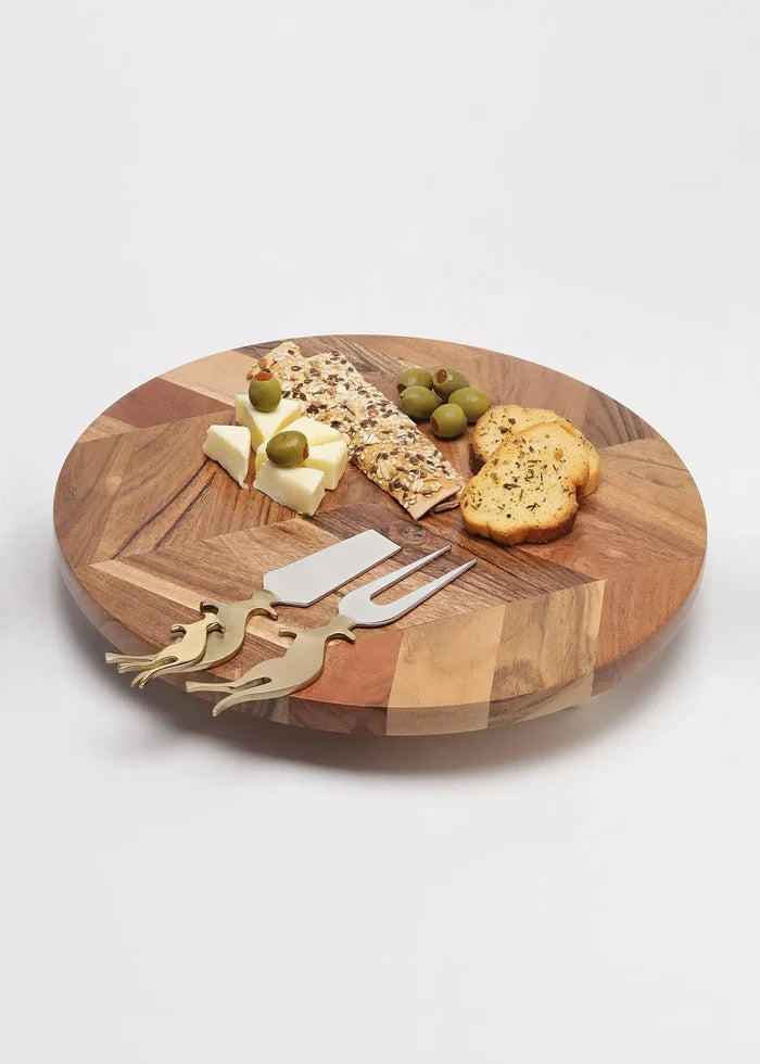 Wooden cheese board with cheese, crackers, and utensils on a white background