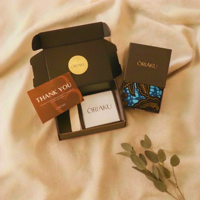 Oriaku product set with a box, card, and pouch on a beige fabric background.