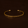 Gold bracelet with engraved details on a dark brown background