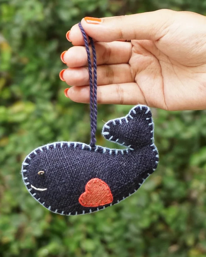 Hand holding a whale-shaped ornament with a red heart on a blurred green background