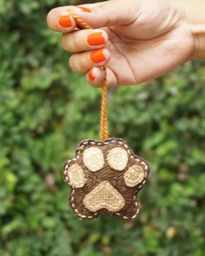 Hand holding a paw-shaped ornament with a blurred green background