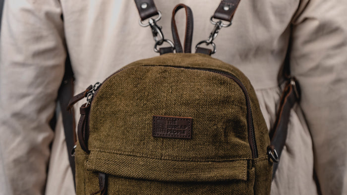 Green backpack with leather straps worn by a person in a neutral background