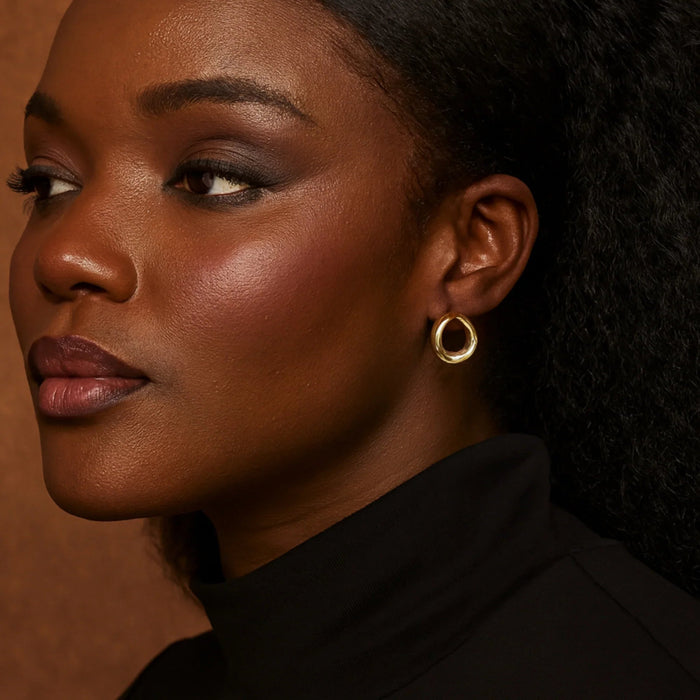 Close-up of a woman wearing gold hoop earrings against a brown background